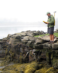 Man stands on rocky shore with GPS unit.