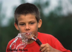 photograph of boy drinking water from a hose