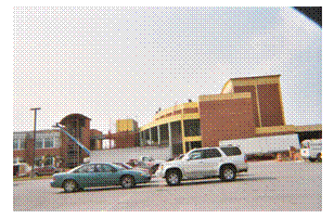 A parking area is in the foreground and a two story building in the right background. In the left background is a two story building with some trailers and a crane in front of them.
