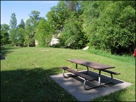 A picnic table sits on a green grassy lawn beneath a towering white sandstone bluff.