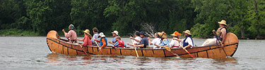 Re-enactors in a large birchbark Voyageur canoe paddle the Mississippi River.