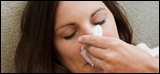 Photo: A woman wiping her nose with a tissue.