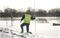 Man measuring water and ice levels along riverbank.