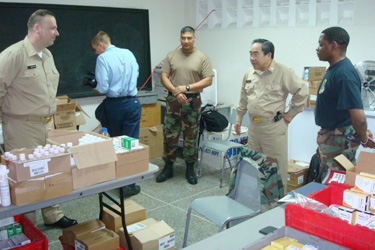 Acting Surgeon General RADM Kenneth P. Moritsugu visits the temporary provider site Moulton Methodist School in Trinidad and speaks with pharmacy personnel.   LCDR Andrei Nabakowski is on the far left.