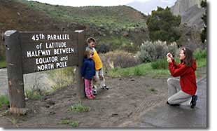 A family takes pictures in front of a sign marking the 45th parallel of latitude.