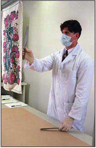 Photograph of a Trace Evidence Unit scientist removes debris from a piece of cloth.  The debris will be preserved for further analysis