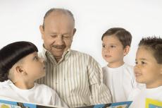 Fotografía de un hombre mayor leyéndoles un libro a tres niños