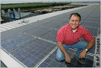 Man kneeling on roof covered with solar panels (AP Images)