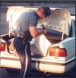 Photograph of a police officer searching a vehicle's trunk