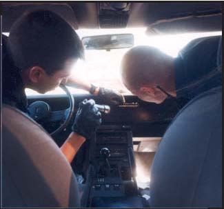Photograph of two police officers searching the glove box of a vehicle