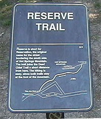 color photo of Reserve Trail trailhead sign. Sign is made of dark brown metal with gold lettering and map of trail