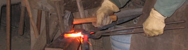 Gloved hands hammer a red-hot piece of steel against and anvil.