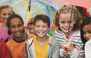A
group of kids crowded together holding umbrellas.