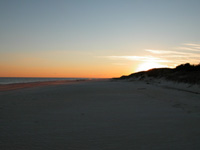 Sun sets behind dark silhouette of dune.