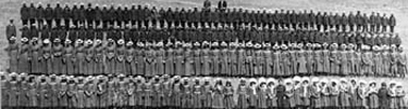 Indian Boarding School at Fort Spokane: Black and white photo. Students in uniform in four long lines. Girls in dresses in front two rows.