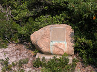 Bronze marker embedded into reddish stone beside trail.