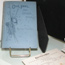 Notebook with handwritten diary entries lies open in front of the portrait of a well-dressed woman from the late 1800s.