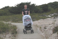 Woman pushes net-covered stroller down a concrete path through dunes.