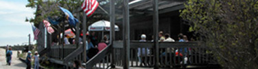 People enter deck to Sailors Haven Snack Bar, bordered by flags and umbrellas.