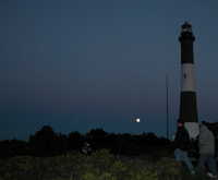 Group walks to bayside beach in front of Fire Island Lighthouse, with moon rising in background.