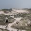 Lone hiker walks faint trail through dunes.