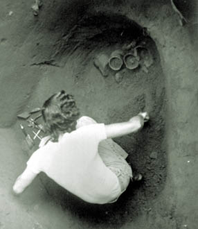 [NPS photo] Archeologist works  in pit to recover pots.