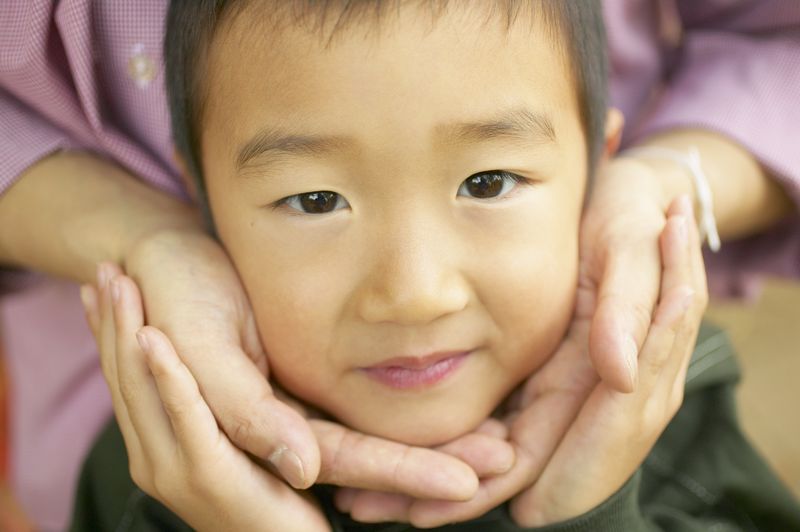 A young Asian boy, his face cupped in caring hands.