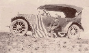 Sepia tone historic photograph of Homer Farr sitting on the running board of his flag draped Model T.