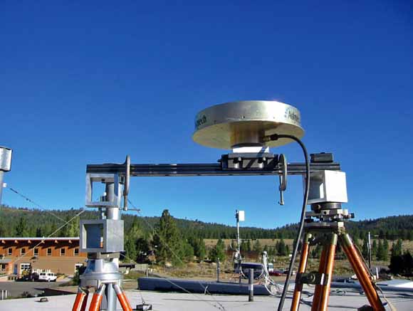 Photo of GPS device on beam between two tripods; sparce lodgepole-pine forest on volcanic soil in background