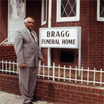 Carnie Bragg next to a sign reading 'Bragg Funeral Home'