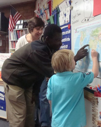 Photo fo a YES student from Ghana pointing out his country on a map to a young American child..