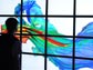 A young man stands in front a bank of computer monitors that project a simulation of river currents.