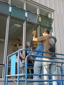 Four individuals, two on the exterior, two inside, installing one of the 15 smaller windows within a picture window.