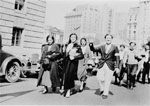 People walking down a street, with tall buildings behind them