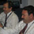 This photo shows Todd Bayer and Dan Johnston, both wearing white shirts, ties, and headsets, laugh and smile over the successful launch.  Todd is putting the cap on a water bottle, and Dan is flipping through a flight plan.