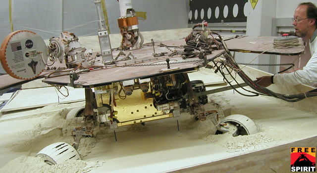 In this view from behind a test rover, the rear wheels of the rover are turned toward the left, and the left-front wheel is turned toward the the right.