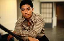 Latino man leaning against a piece of furniture in a living room.