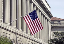 Image of flag flying from facade of U.S. Department of Commerce's Herbert Clark Hoover Building