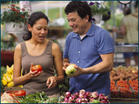 Photo - A man and women selecting vegetables in a supermarket produce area.