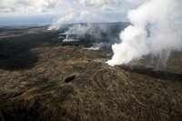 View of the east rift zone eruption site from vent to ocean entry. The TEB vent, where the lava erupts and enters the lava tube system, is the large fume source in foreground. The prominent plumes in the background are the ocean entries, with the larger Waikupanaha entry to the left of the smaller Kupapa`u entry. The smaller fume sources between the vent and the ocean entries define the trace of the lava tube system carrying lava across the upper flow field.