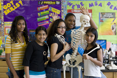 Female students posing with skeleton in a classroom
