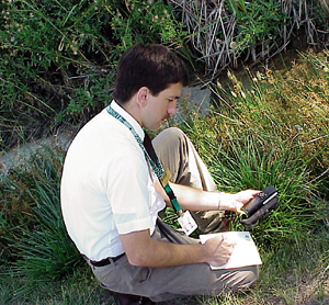 A color photograph showing a man sitting in a field working with GPS receiver.