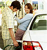 A man pumping gas while talking to a woman.