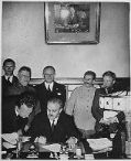 Soviet Foreign Minister Vyacheslav Molotov signs the Molotov-Ribbentrop Pact. Behind him stand (left) German Foreign Minister Joachim von Ribbentrop and (right) Soviet Premier Joseph Stalin.