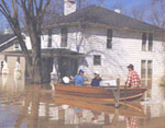 Image of 3 men in a boat in front of a flooded house
