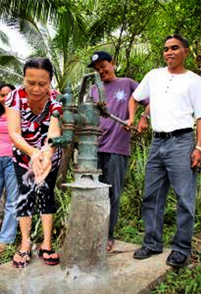 Binoni Elementary School PTCA president Ladyluz Maglangit (left) washes her hands at the newly installed water pump in the school, as principal Celso Reambonanza (right) and barangay chairman Eldy Paghasian (middle) look on. The pump is part of the PTCA’s water system project that was completed last month with an EQuALLS2 community grant.