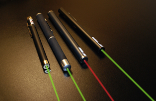 four laser pointers on a dark background with visible laser light coming out