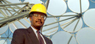 Photo of a man in a suit wearing a hard hat standing in front of a solar dish generator.