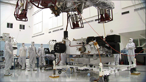 These three images show the progression of 'stacking' the Mars Science Laboratory rover and its descent stage in one of the Jet Propulsion Laboratory’s 'clean room.'  In the first image, the car-size rover is in the middle of the picture with several team members surrounding it.  The team members are all dressed in special head-to-toe white suits, called 'bunny suits.'  One team member is holding on to a tether to guide the large insect-like descent stage down on top of the rover.  The descent stage looms high in this image.  The second image shows the descent stage a few feet above the rover with the team member continuing to guide the two pieces together.  The final image shows the two pieces on top of each other.