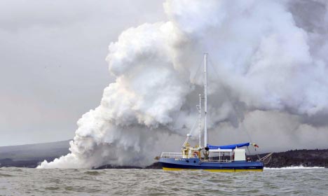 Godfrey Merlen aboard his little ship Ratty while Fernandina erupts behind him in April 2009.